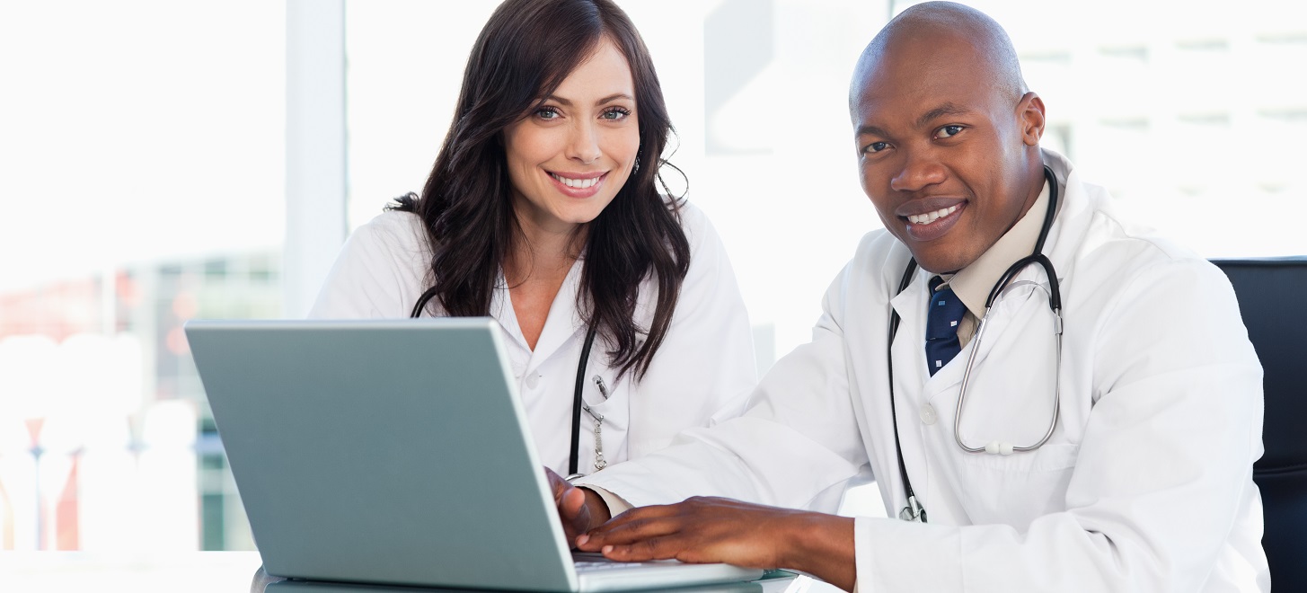 Smiling medical staff working in front of a laptop while sitting at the desk Medical staff working in front of a grey laptop while sitting at the desk
