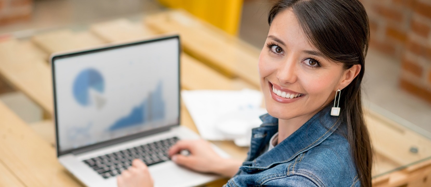 Graphic designer working at the office Happy female graphic designer working at the office using her laptop and looking at the camera smiling