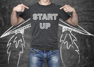 A businessman is pointing out in the chest where is a word collocation ' start up '. A concept of the starting up new business. Drawn wings. Black chalk board on the background. A businessman is pointing out in the chest where is a word collocation ' start up '. A concept of the starting up new business. Drawn wings. Black chalk board on the background.